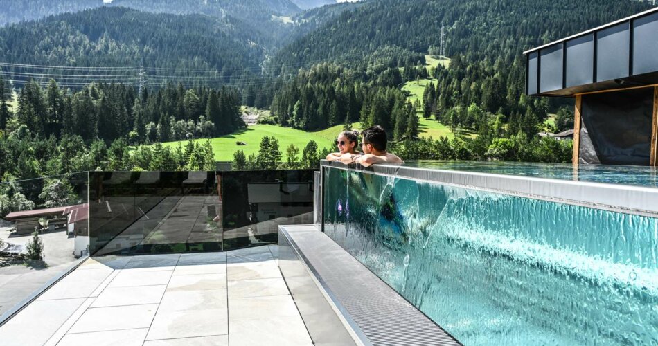 Two people in a modern outdoor pool, with a mountain panorama behind them