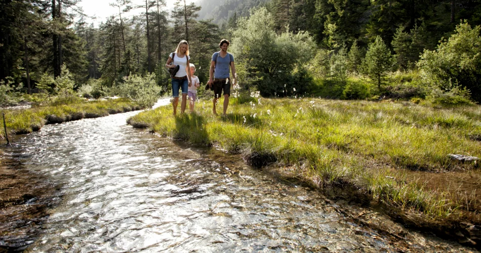 Eine dreiköpfige Familie spaziert an der Loisach entlang. Rund herum lichter Nadelwald und grüne Wiesen mit Blumen.  | © Tiroler Zugspitz Arena_U. Wiesmeier