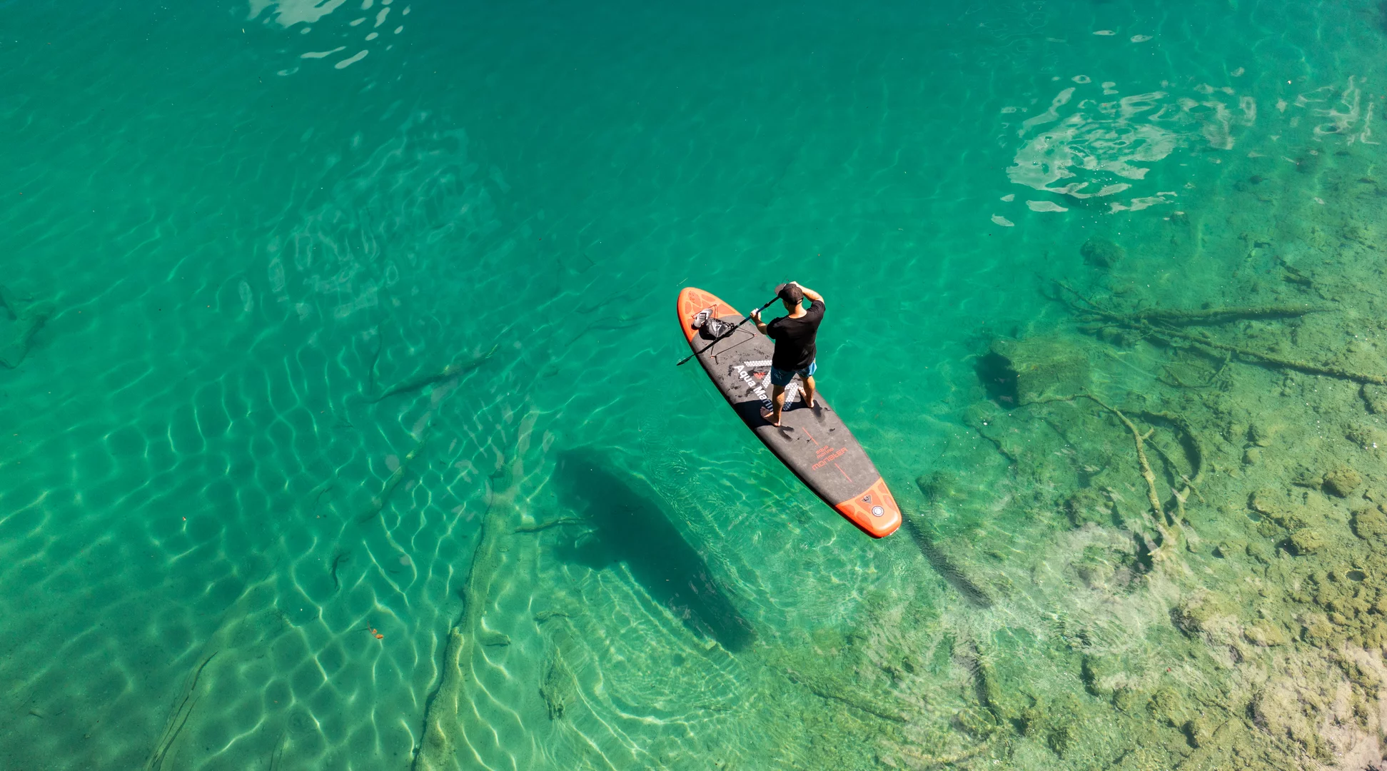 Stand Up Paddle Board | © TZA / Sam Oertiker Stand up paddle board photographed from above on turquoise water. A man is standing on it and paddling. | © TZA / Sam Oertiker
