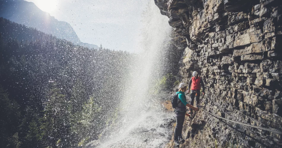Zwei Kletterer die an einem Seil unter dem Wasserfall durch gehen. | © ZABT / T. Jorda