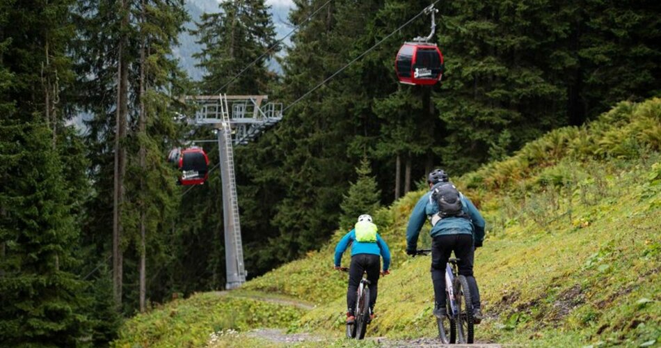 Zwei Mountainbiker auf einem Trail, daneben die Gondeln der Bergbahnen Berwang