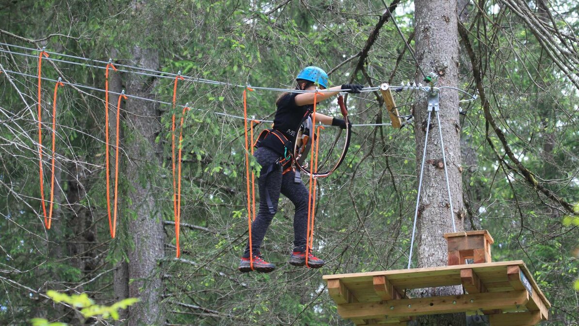 A person climbs an obstacle between trees in the climbing park | © Alpinschule Lermoos