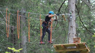 Eine Person klettert im Kletterwald an einem Hindernis zwischen Bäumen | © Alpinschule Lermoos
