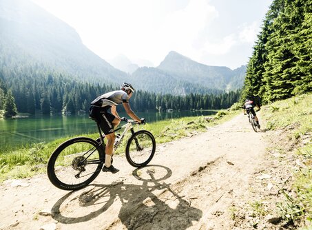 Two mountain bikers ride along a path on the shore of a turquoise mountain lake | © Markus Greber