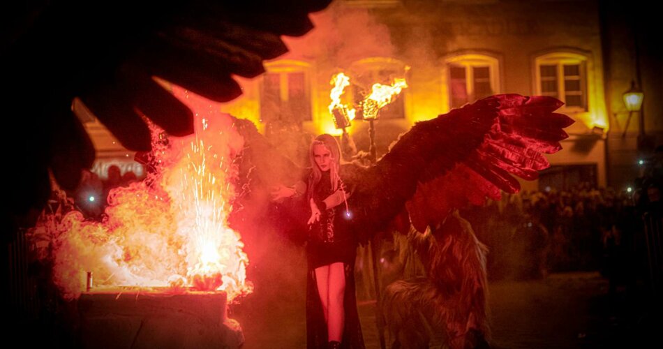 A woman in a scary costume with big black wings, a fire in front of her | © Tiroler Zugspitz Arena/Moos Tuifl Ehrwald