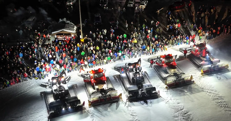 Several snow groomers stand side by side at the edge of the slope, with a large crowd of people in front of them | © Werbeagentur Bärig