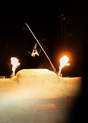 Ein Profi-Skifahrer springt über eine Schanze, daneben Feuer-Show | © Tiroler Zugspitz Arena
