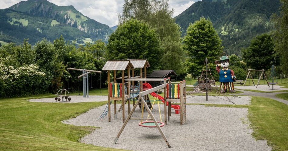 Playground with swing and slide on gravel in front of forest and mountain panorama | © TZA