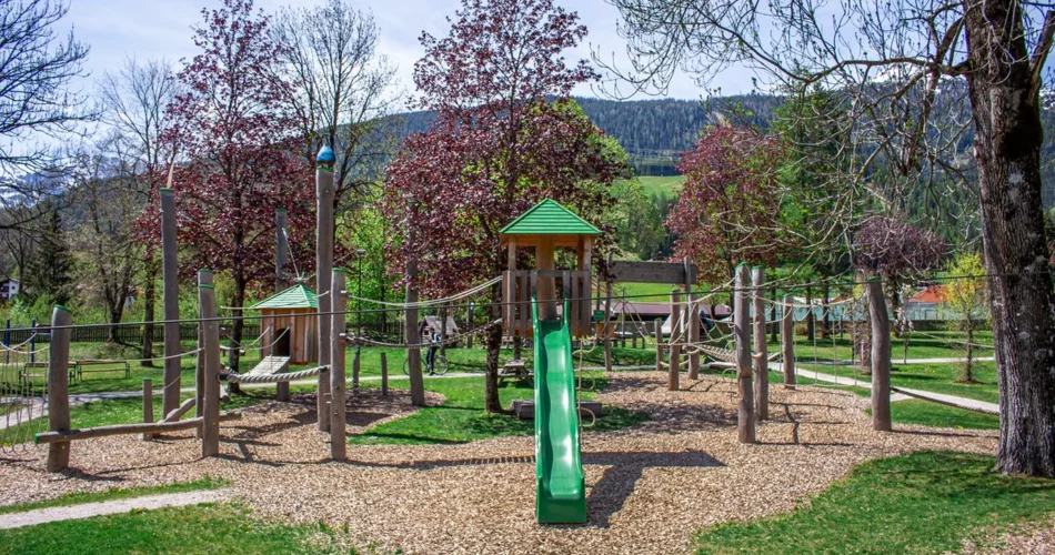 Großer moderner Spielplatz mit grüner Rutsche in mitten von Bäumen | © TZA