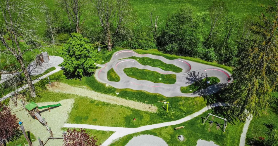 Blick von oben auf den Pumptrack neben einem Spielplatz umgeben von Wiesen | © TZA