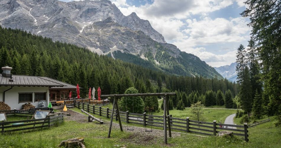Playground with swing next to an alpine hut in front of a mountain panorama | © TZA