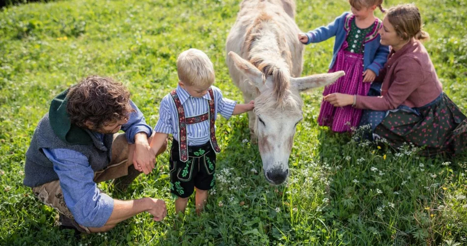 Eltern streicheln mit Ihren Kindern einen Esel auf einer Wiese | © TZA