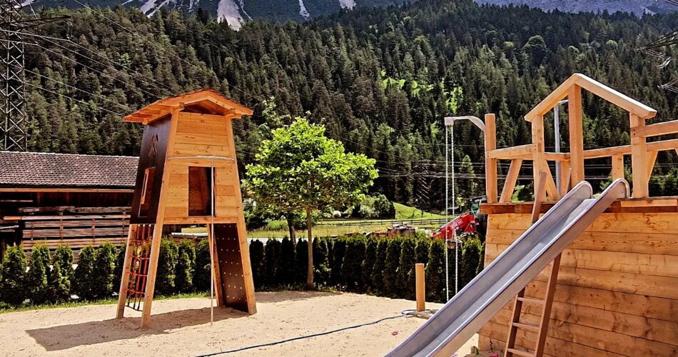 Modern playground on sand with a slide and a climbing frame in front of a mountain panorama | © Basta 11