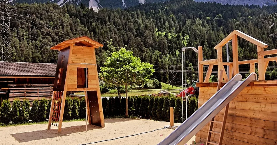 Moderner Spielplatz auf Sand mit einer Rutsche und einem Klettergerüst vor Bergpanorama | © Basta 11