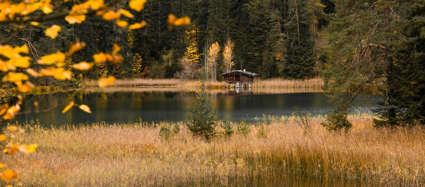 Ein See und eine Holzhütte umgeben von einem herbstlichen Wald | © Tiroler Zugspitz Arena/Bianca McCarty