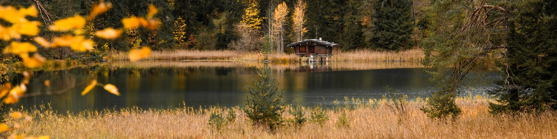 A lake and a wooden hut surrounded by an autumnal forest | © Tiroler Zugspitz Arena/Bianca McCarty