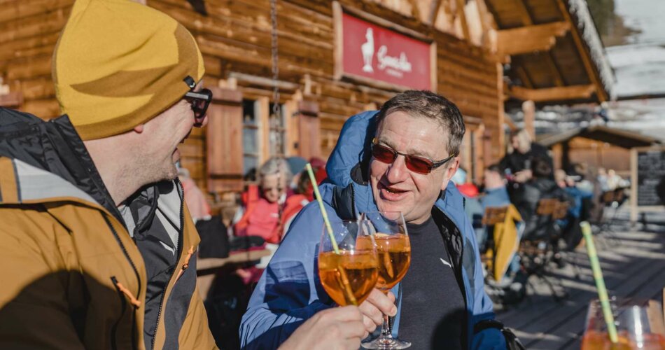 Zwei Männer stoßen auf der Terasse einer Hütte mit einem Getränk an  | © Tiroler Zugspitz Arena/Sam Oetiker