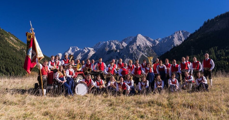 A chapel with traditional Tyrolean costume in front of a mountain panorama | © Musikkapelle Lähn