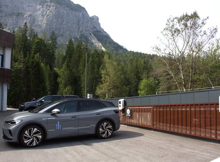 A gray car parked in front of an e-charging station, a mountain in the background | © TZA