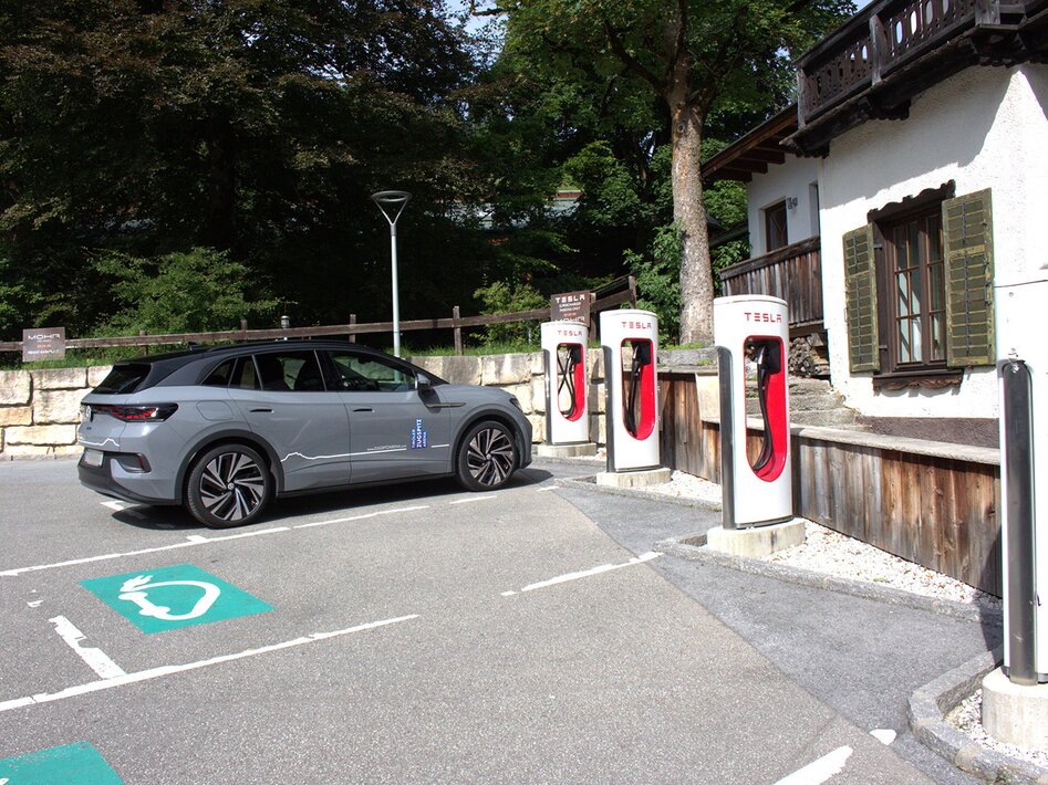 A gray car parked next to several white Tesla e-charging stations | © TZA