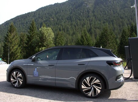 Ein graues Auto neben zwei großen schwarzen E-Ladesäulen, im Hintergrund ein Berg | © TZA