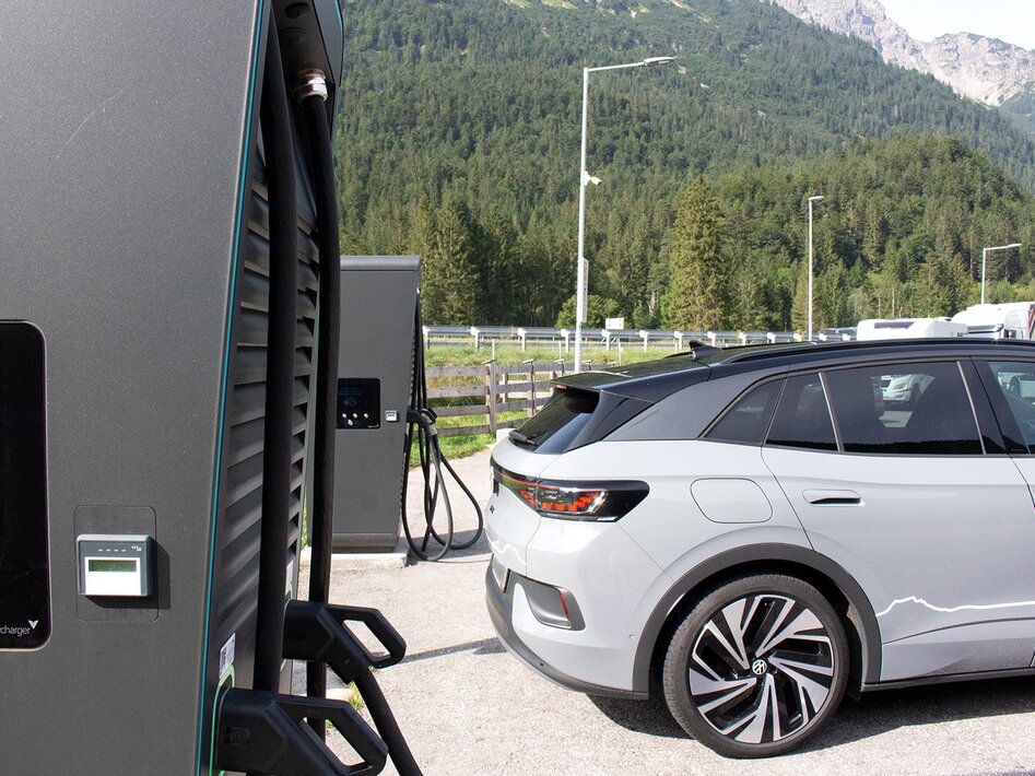 A gray car next to two large black e-charging stations, a mountain in the background | © TZA