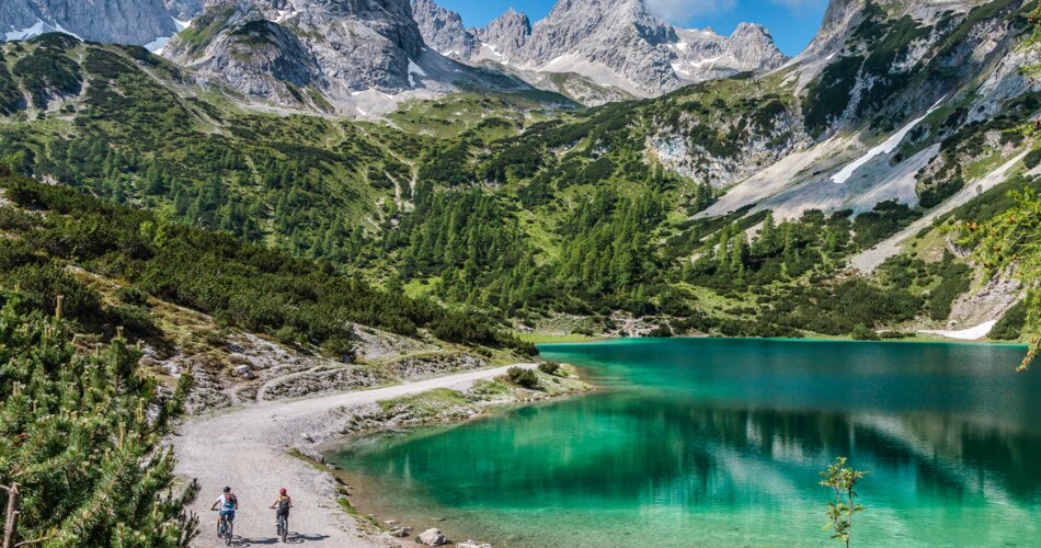 Zwei Mountainbiker auf einem Weg neben dem türkisfarbenen Seebensee, umgeben von beeindruckendem Bergpanorama | © Tiroler Zugspitz Arena