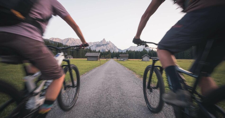 Zwei Radfahrer auf einem Weg, im Hintergrund Wald und Bergpanorama | © Tiroler Zugspitz Arena/C. Jorda