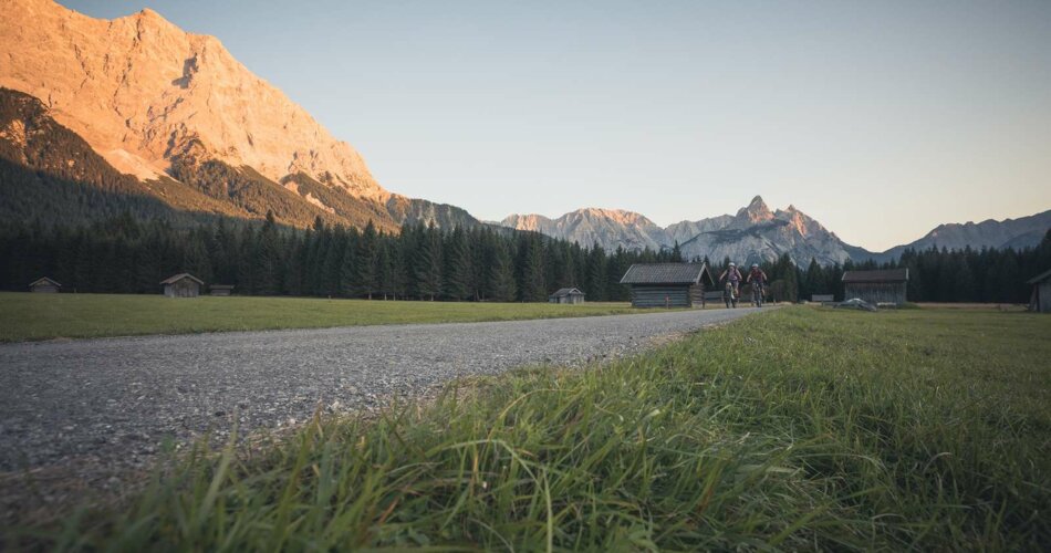 Zwei Radfahrer auf einem Weg, dahinter ein von der Abendsonne angestrahlter Berg | © Tiroler Zugspitz Arena/C. Jorda