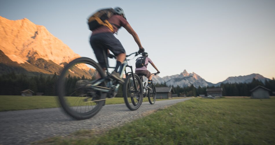 Two cyclists on a path, behind them a mountain illuminated by the evening sun | © Tiroler Zugspitz Arena/C. Jorda