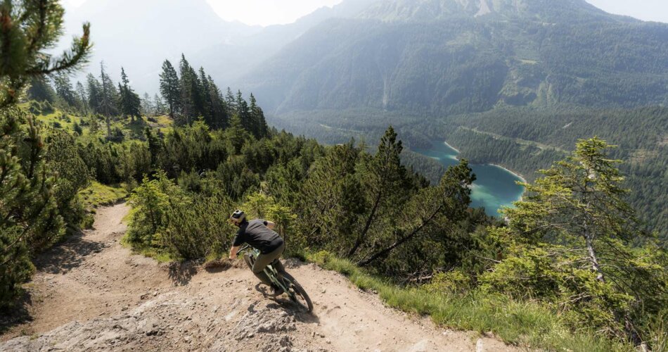 A cyclist on a downhill trail, with Blindsee lake in the background | © KLEMENS KOENIG