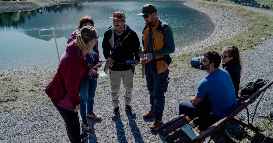 A group solves a puzzle of the escape trail, with a small lake in the background