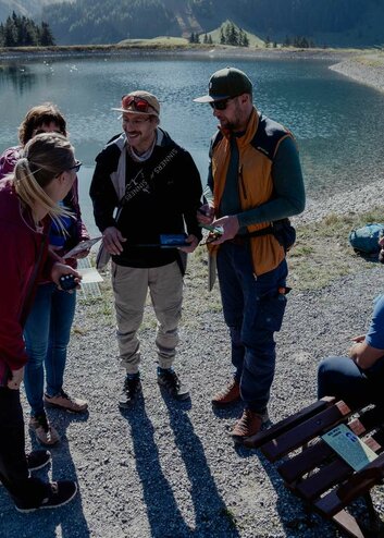 A group solves a puzzle of the escape trail, with a small lake in the background