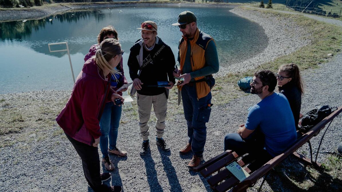 A group solves a puzzle of the escape trail, with a small lake in the background