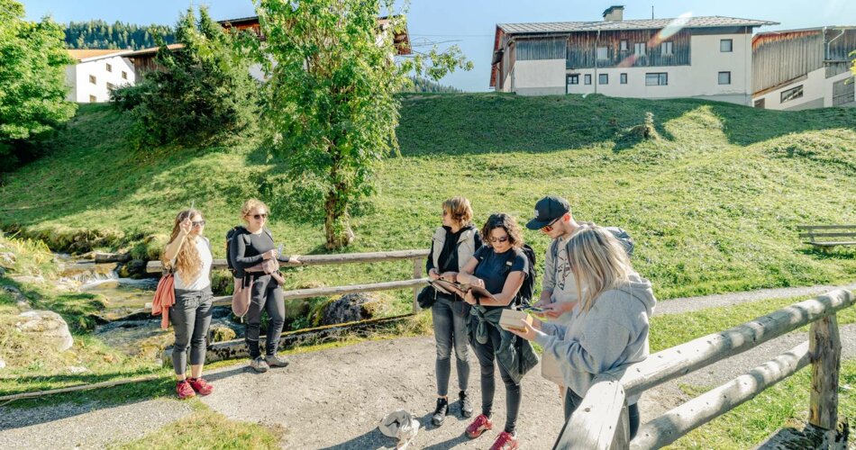 Eine Gruppe steht auf einer Brücke, welche über einen kleinen Bach führt. Sie sind dabei gemeinsam ein Rätsel zu lösen. | © Tiroler Zugspitz Arena/Schennach Valentin