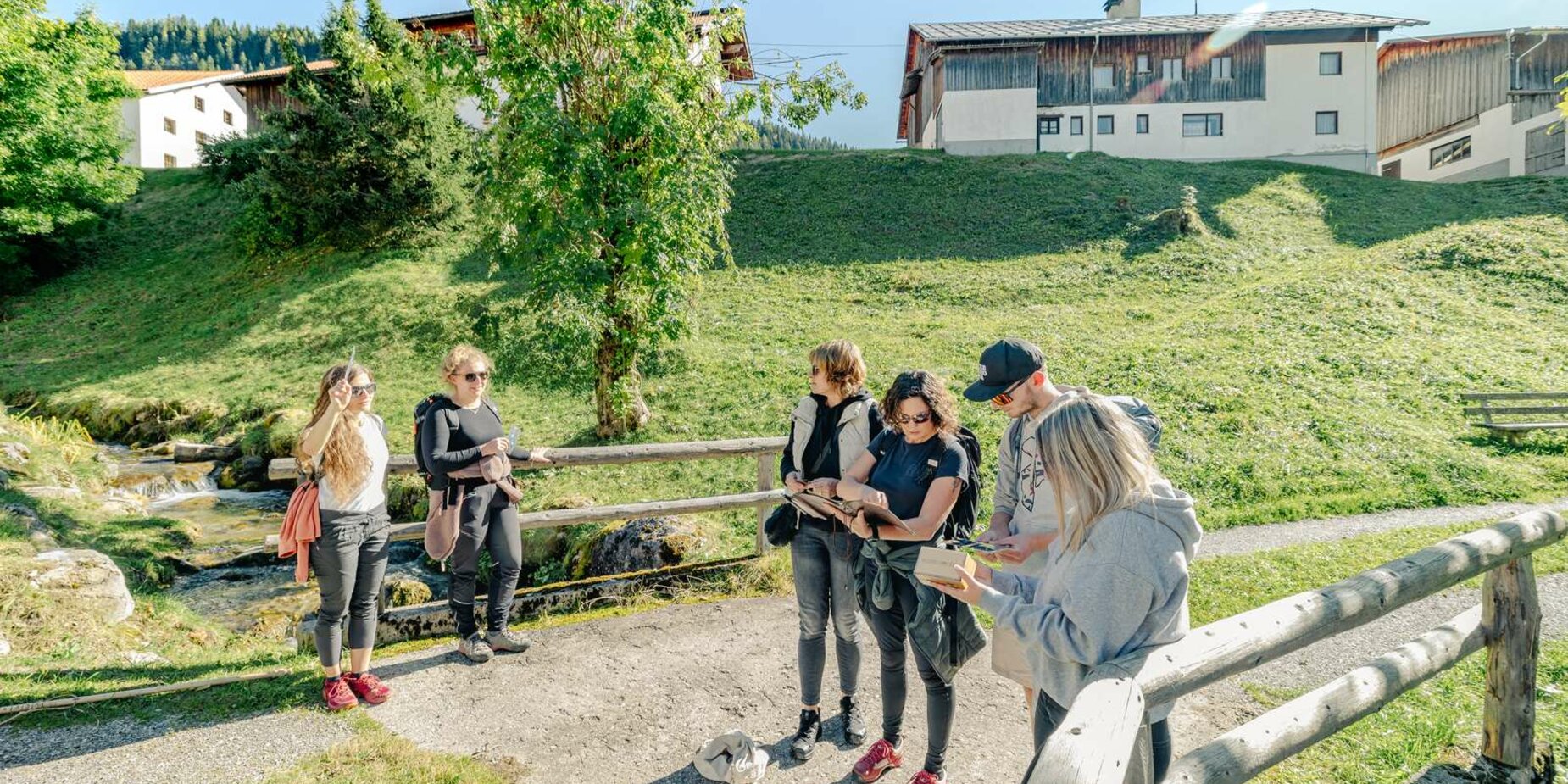 Eine Gruppe steht auf einer Brücke, welche über einen kleinen Bach führt. Sie sind dabei gemeinsam ein Rätsel zu lösen. | © Tiroler Zugspitz Arena/Schennach Valentin
