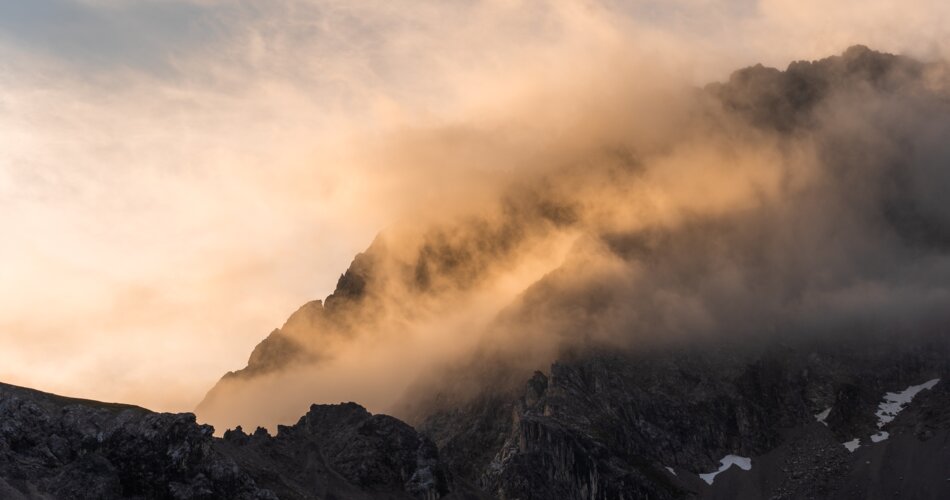 Ein Berg ist in Nebelschwaden gehüllt und wird in orangefarbenem Licht getaucht | © TZA/ Sam Oetiker