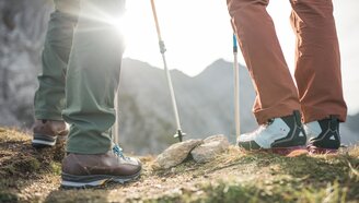 The legs of two hikers, with long hiking pants and hiking boots, next to them, the hiking poles | © Tiroler Zugspitz Arena/C. Jorda