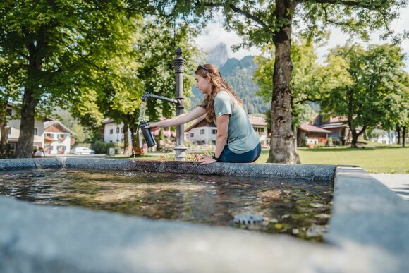 Eine Frau füllt eine Wasserflasche an einem Brunnen auf. | © Tiroler Zugspitz Arena/Sam Oetiker