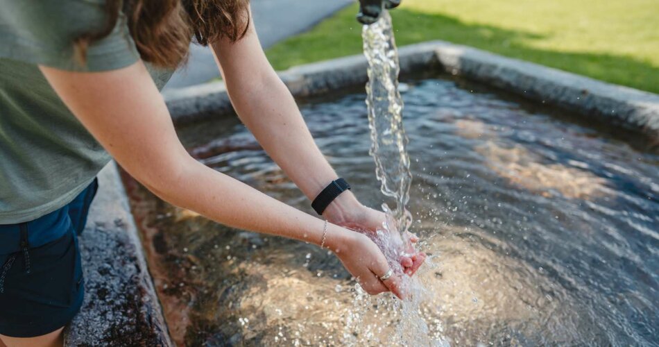 Eine Frau frischt sich an einem Brunnen ab. | © Tiroler Zugspitz Arena/ Sam Oetiker