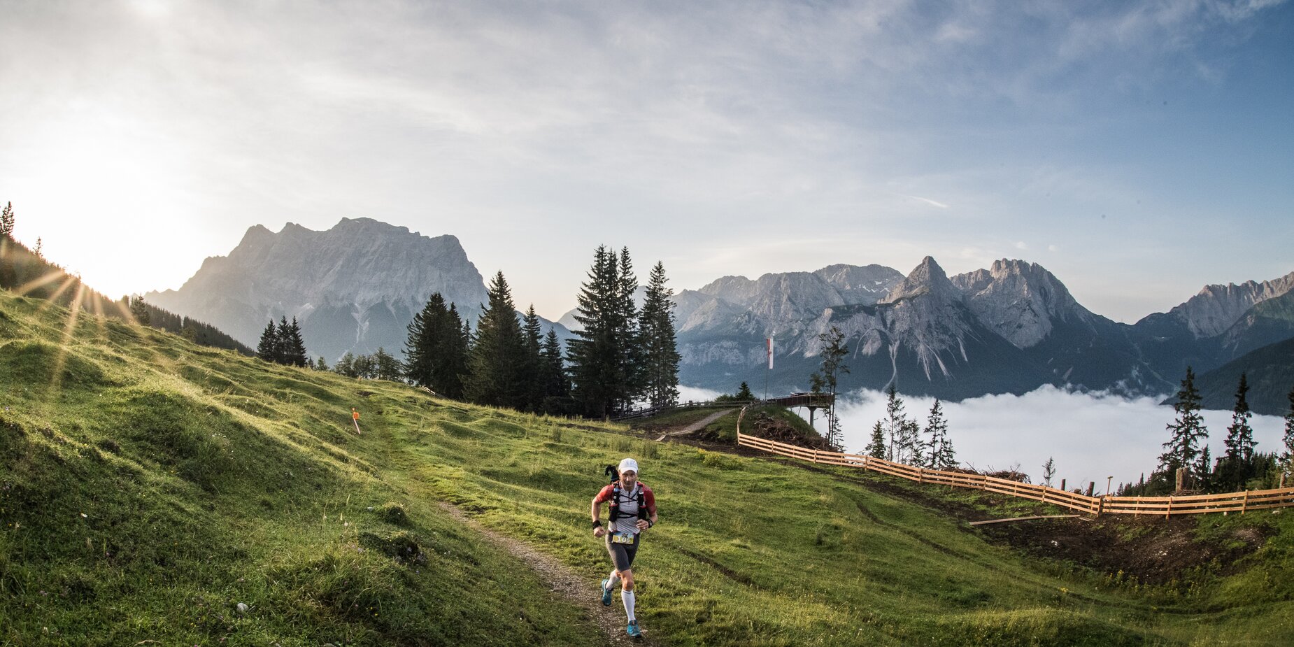 Ein Mann läuft auf einem Weg durch eine Bergwiese. Im Hintergrund Bergpanorama mit der Zugspitze. | © Harald Wiesthaler