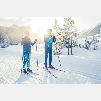 Zwei Langläufer auf einer frisch präparierten Loipe. Im Hintergrund eine verschneite Winterlandschaft, welche von der aufgehenden Sonne angestrahlt wird. | © Tiroler Zugspitz Arena/C. Jorda