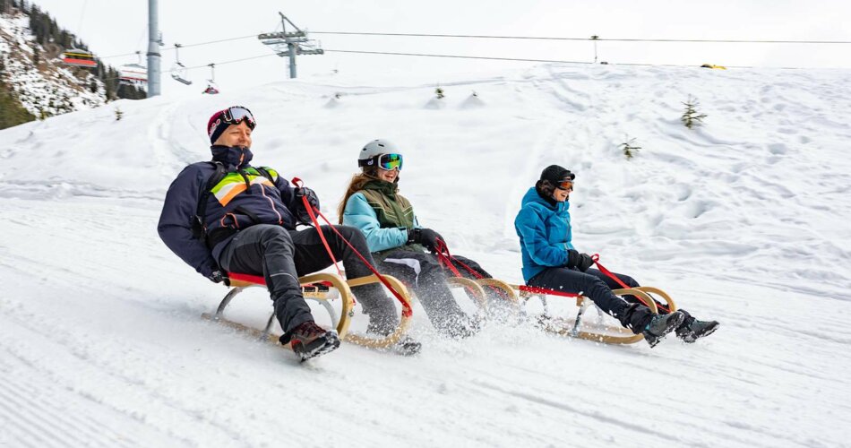 Eine Familie beim Rodeln in Berwang, sie fahren den Berg hinunter, lachen und haben Spaß | © Tiroler Zugspitz Arena/ Valentin Schennach