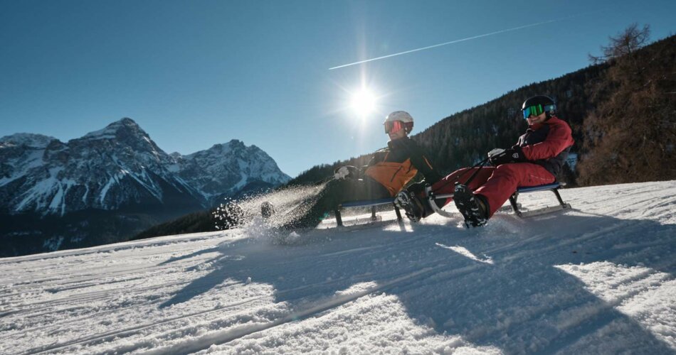 Two tobogganists ride down a toboggan slope, the sun is shining, snow-covered mountains can be seen in the background | © Tiroler Zugspitz Arena/Oostenrijk TV