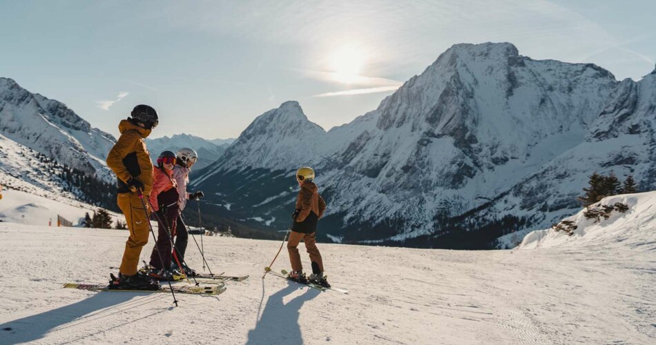 A family doing skiing, they stand on a wide, freshly groomed slope, a high mountain in the background | © Tiroler Zugspitz Arena/Sam Oetiker