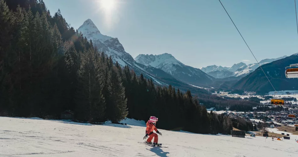 Ein kleines Kind beim Skifahren, im Hintergrund Bergpanorama bei sonnigem Wetter | © Tiroler Zugspitz Arena/Sam Oetiker