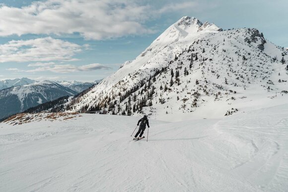 Ein Skifahrer auf einer frisch präparierten Piste, im Hintergrund winterliches Bergpanorama und blauer Himmel | © Tiroler Zugspitz Arena/Sam Oetiker