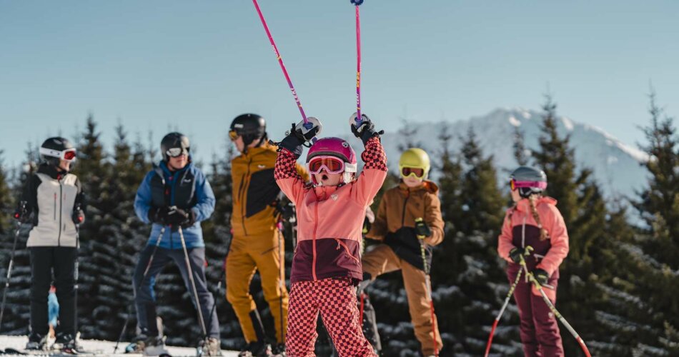 Ein Kind auf Skiern freut sich und hebt die Stöcke in die Luft, dahinter ist die Familie zu sehen | © Tiroler Zugspitz Arena/Oetiker Sam