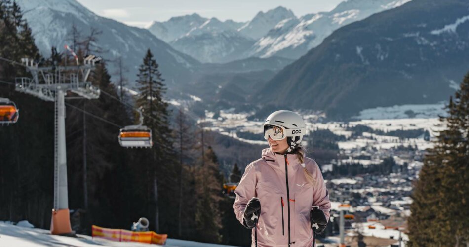 A smiling woman on a ski slope, a chairlift and a wintry mountain panorama in the sunshine in the background | © Tiroler Zugspitz Arena/Sam Oetiker