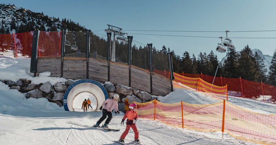 Eine Familie fährt mit Skiern durch einen Tunnel in der Funslope im Skigebiet Ehrwalder Alm | © Tiroler Zugspitz Arena/Sam Oetiker